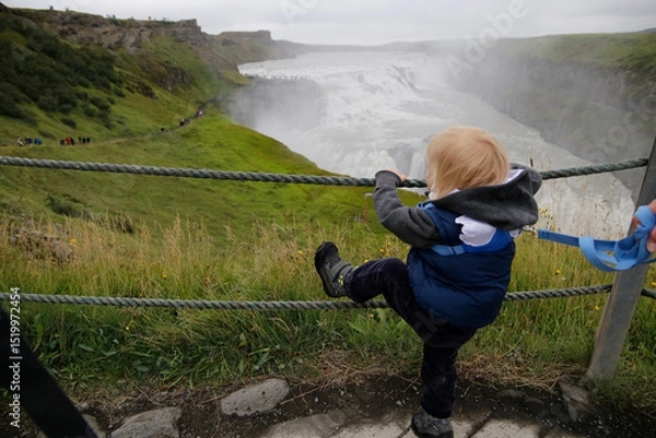 Obraz Small child on a safety leash climbing railing while observing the powerful Gullfoss waterfall in Iceland.