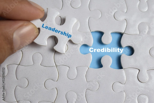 Obraz Hand holding piece of jigsaw puzzle with word Credibility and leadership. Business and finance concept