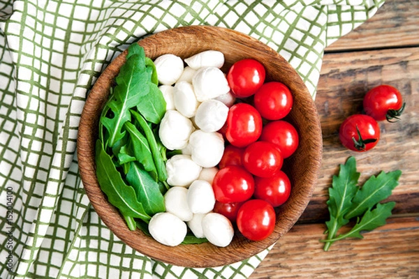 Fototapeta Flag of Italy from ingredients for vegetarian healthy salad - cherry tomato, mozzarella cheese and arugula on a wooden plate. Old dark wooden table background with napkin.
