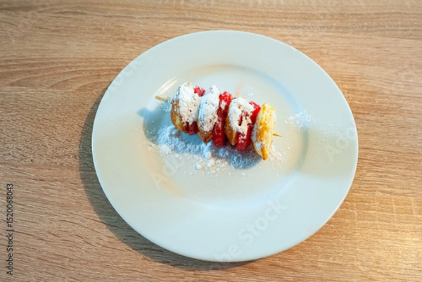 Obraz Plate with traditional dutch batter cakes and strawberry slices on a stick, sprinkled with powdered sugar