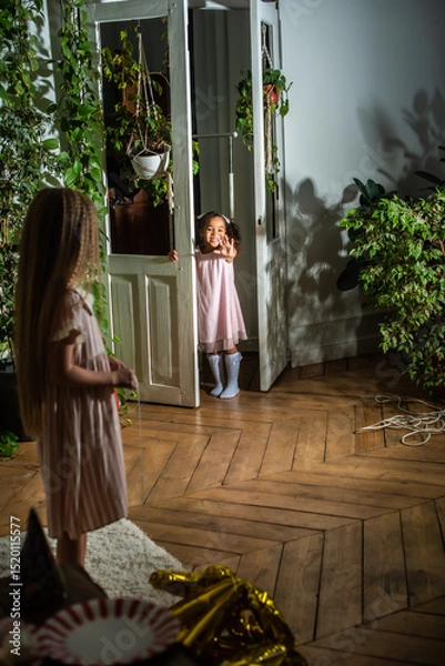 Obraz A little girl wearing a lovely pink dress is standing happily in front of a door, waving to another child