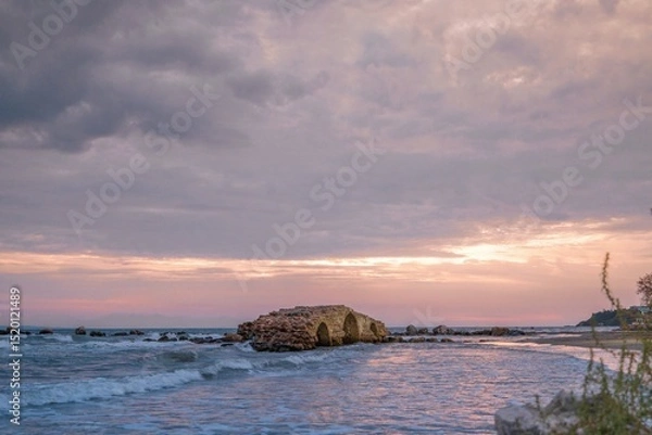 Obraz A stunning sunset casts a warm glow over the serene waters of Zakynthos, highlighting the remnants of an ancient structure by the shore