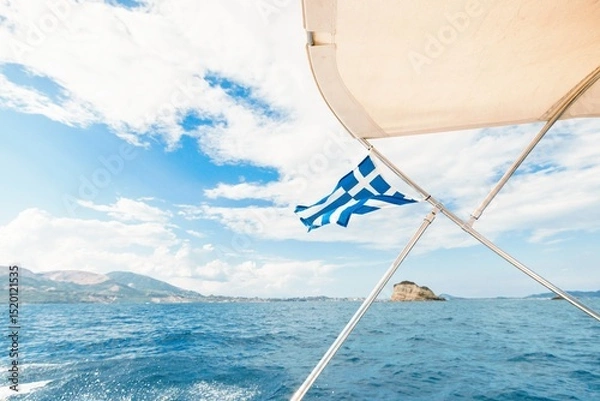 Obraz Gliding across the sparkling blue waters near Zakynthos, a Greek flag flutters on the boat as sunlight sparkles off gentle waves. The breathtaking landscape invites adventure and exploration