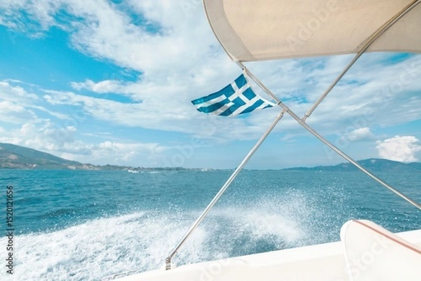 Obraz Tourists enjoy a serene boat ride in Zakynthos, with the vibrant Greek flag waving against a backdrop of shimmering blue seas and fluffy white clouds in summer