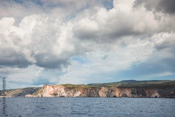 Obraz Waves gently lap against rock formations as dramatic clouds dance overhead in Zakynthos, where summer tourism brings vibrant energy to the stunning coastal landscape and azure sea