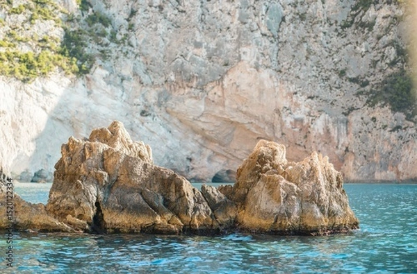 Obraz Sparkling turquoise waters gently lap against rugged rock formations in Zakynthos, as summer tourists savor the beauty of this stunning coastal paradise, perfect for adventure and relaxation