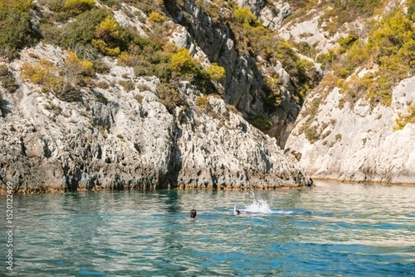 Obraz In the warm sunlight, two swimmers enjoy the crystalline waters of Zakynthos, surrounded by stunning rocky cliffs and lush greenery. A perfect summer escape awaits