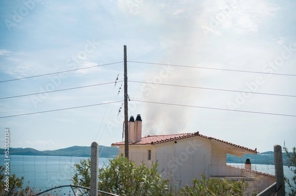 Obraz A serene summer day in Zakynthos showcases a quaint home by the sea, with smoke gently wafting from its chimney. This scene captures the essence of laid-back island life, embraced by azure waters