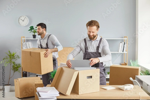 Fototapeta Moving delivery pack service, male movers team moving cardboard boxes, loading, unloading setting up of household goods, new house stuff, carrying stacks of cardboard relocation boxes in office room