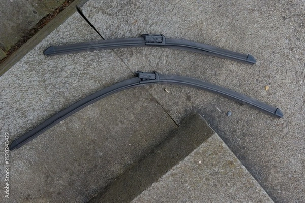Fototapeta Two sleek, dark wiper blades rest on a textured concrete surface, highlighting their robust design and readiness for clear vision.