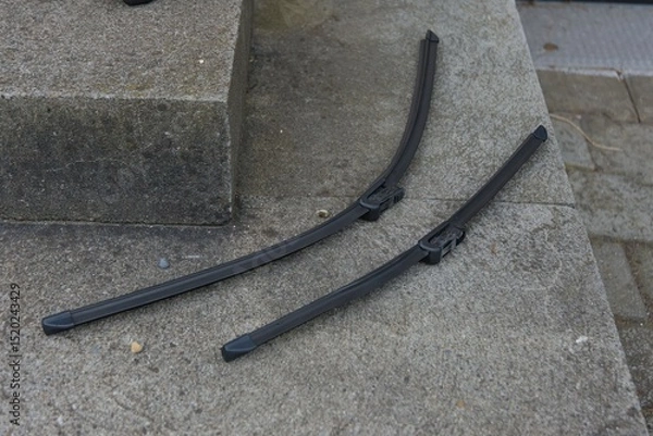 Fototapeta Two sleek, dark wiper blades rest on a textured concrete surface, highlighting their robust design and readiness for clear vision.