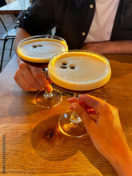 Obraz Hands Clinking Espresso Martinis at Golden Hour in Cozy Café Setting