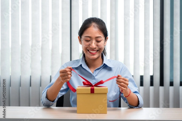 Obraz Happy woman is smiling and holding present box to wrapped with red ribbon while preparing gift for celebrate