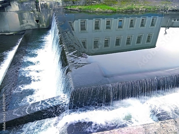 Fototapeta Reflection of architecture in the mirror of the water surface. Movement of the river in the urban development. River dam. Postcard. Cover. Wallpaper