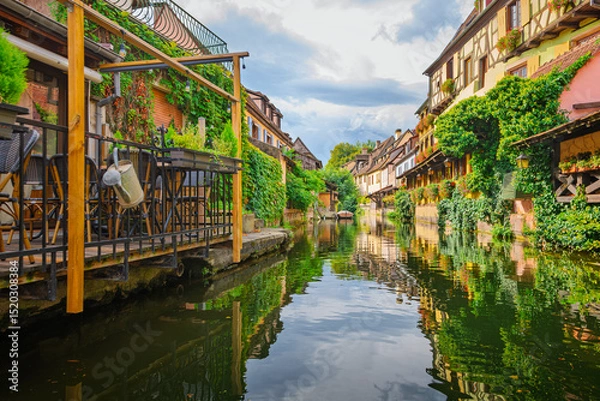 Fototapeta Water level view from a boat as it passes by half timbered colorful historic buildings along the Lauch Canal in the historic Petite Venise district of Colmar, France.