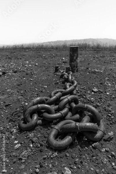 Obraz Rusty chain anchored to a weathered post in a desolate landscape