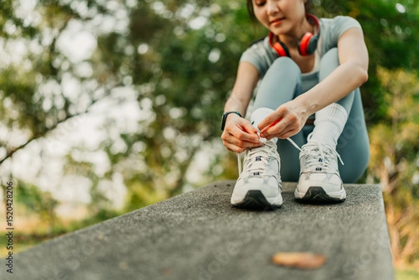Fototapeta A woman dressed in workout clothes is tying her shoelaces, preparing to go for a run and exercise at the park.