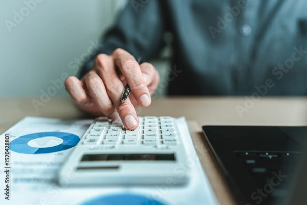 Fototapeta An accountant is seated at a desk in the office, utilizing a calculator to determine balances, profits, currency conversions, and costs. This involves various accounting and financial concepts.