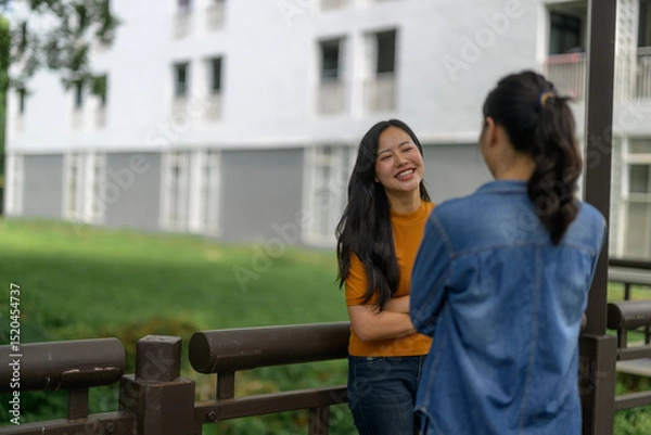 Fototapeta Two young women chatting and smiling near a railing in a university campus
