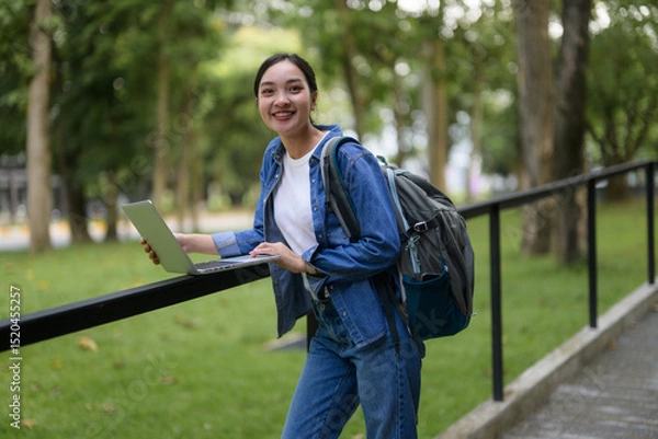 Fototapeta Smiling student using laptop in university campus park