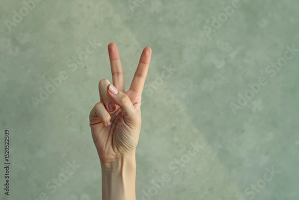 Obraz hand displays a peace sign with two fingers raised against a muted green background.