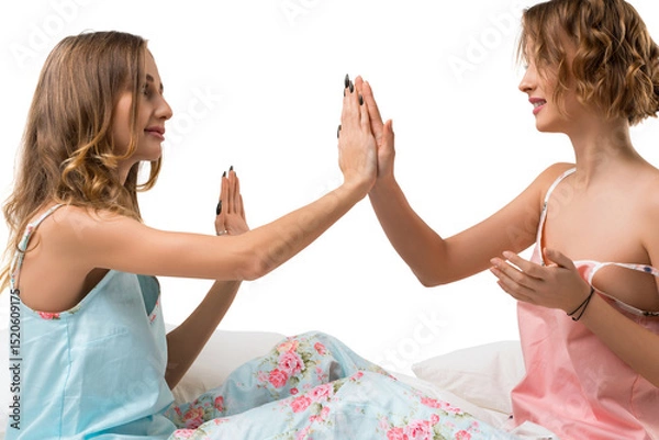 Fototapeta Two friends playing a hand game while lounging on a bed in casual outfits