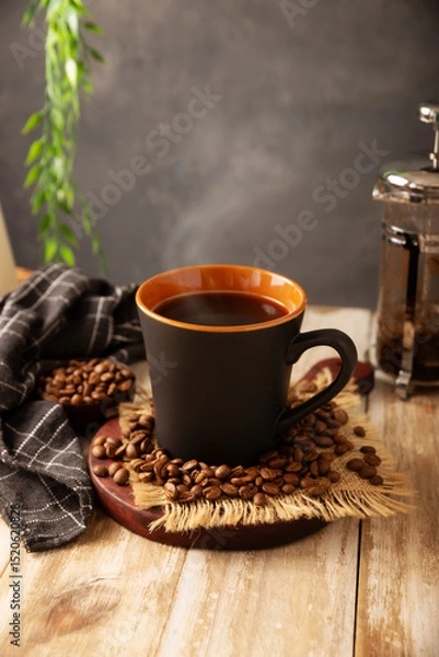 Fototapeta Black coffee in a black cup with coffee beans on rustic wooden table, french press on background.