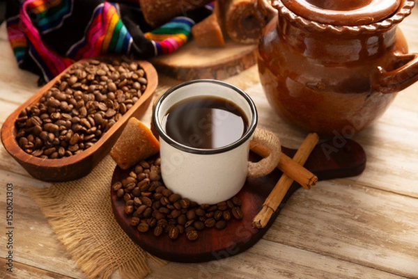 Fototapeta Cafe de Olla. Traditional Mexican coffee and basic ingredients for its preparation, coffee, cinnamon and piloncillo, served in a metallic cup called "peltre" on a rustic wooden surface.