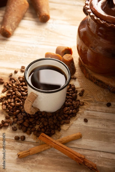 Fototapeta Cafe de Olla. Traditional Mexican coffee and basic ingredients for its preparation, coffee, cinnamon and piloncillo, served in a metallic cup called "peltre" on a rustic wooden surface.
