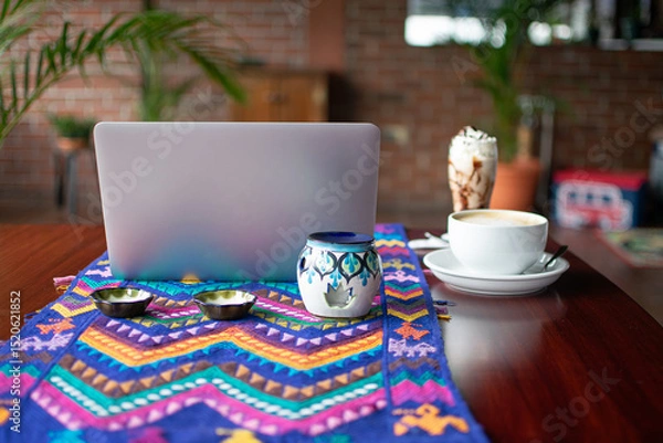 Fototapeta Photograph of a chocolate milkshake cocktail and a large cup of coffee next to a laptop on a table with a textile-patterned tablecloth, front view.