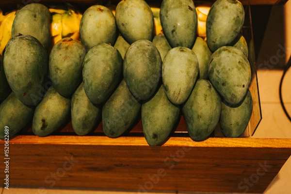 Fototapeta Large green mango on the counter in a supermarket. Exotic fruits in a fruit shop