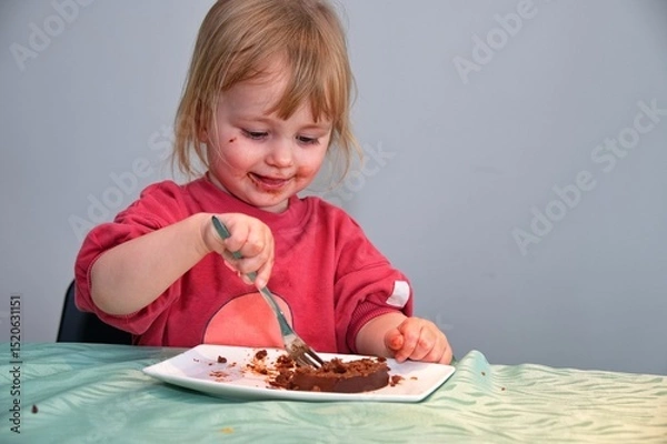 Obraz Little girl sitting at the table and eating chocolate cake