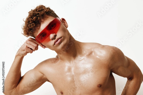 Fototapeta Confident shirtless young man posing with red sunglasses, showcasing a strong physique against a neutral background. Fashion and self-expression concept.