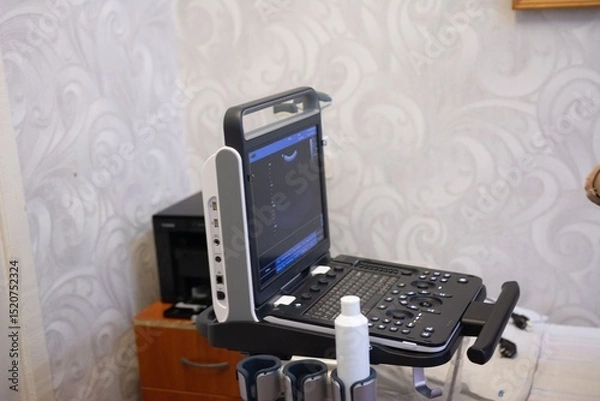 Fototapeta An ultrasound machine with a screen, keyboard, and a bottle of gel is positioned in a clinical setting, ready for diagnostic imaging.