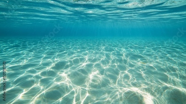 Fototapeta Underwater view shows sunlight filtering through clear turquoise water onto sandy bottom.