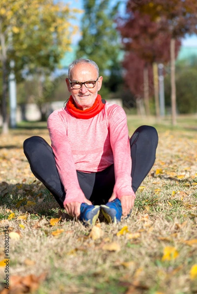 Fototapeta Senior man stretching on the grass during outdoor exercise