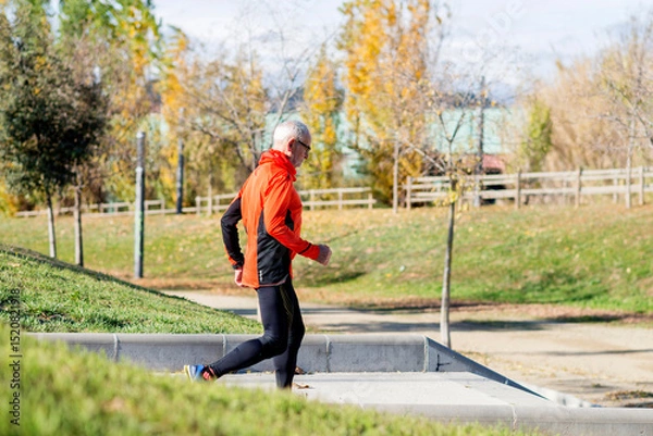 Fototapeta Senior man running up stairs in an outdoor park setting
