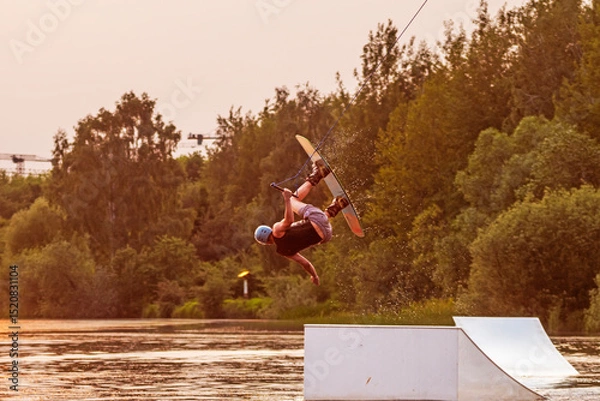 Obraz Wakeboarder making tricks. Low angle shot of man wakeboarding on a lake. Man water skiing at sunset.	