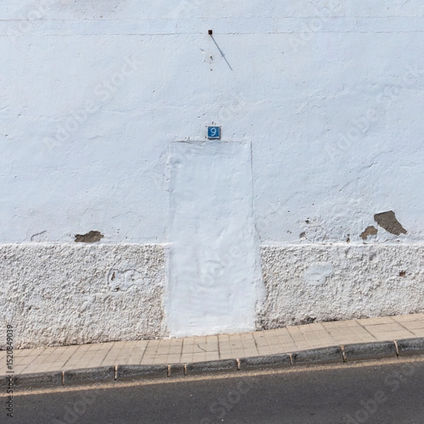 Fototapeta White wall with a bricked-up door, painted over, creating a seamless appearance. Above the door is a blue ceramic sign with the number &quot;9.&quot;