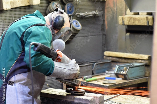 Fototapeta Worker with a grinding machine machines a workpiece made of steel in an industrial company - work safety with ear and eye protection