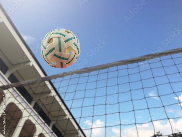 Fototapeta Lookup view image of a yellow plastic sepak takraw ball which floats above the net in the outdoor sepak takraw court, soft and selective focus on ball.