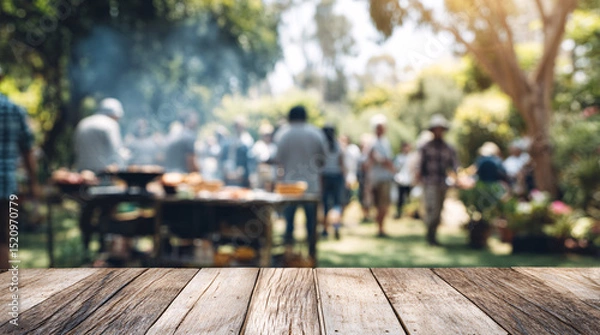 Fototapeta Wooden table surface with blurred outdoor barbecue party background and people gathering. Empty deck space for product display against social dining setting