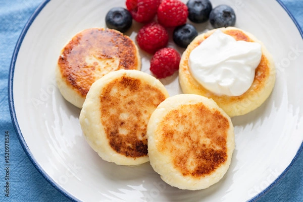 Fototapeta Syrniki, curd cheese fritters with berries and sour cream closeup view