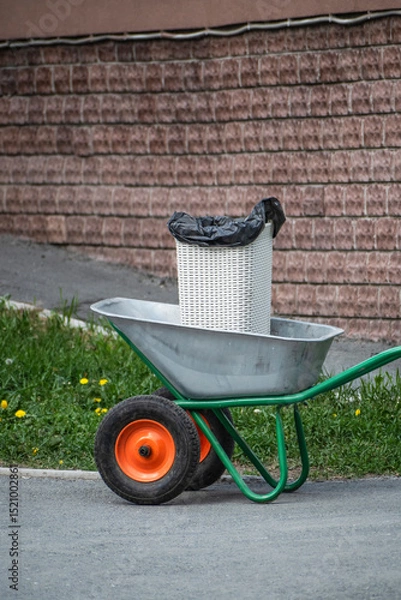 Fototapeta A wheelbarrow with a trash can on the sidewalk on a summer day