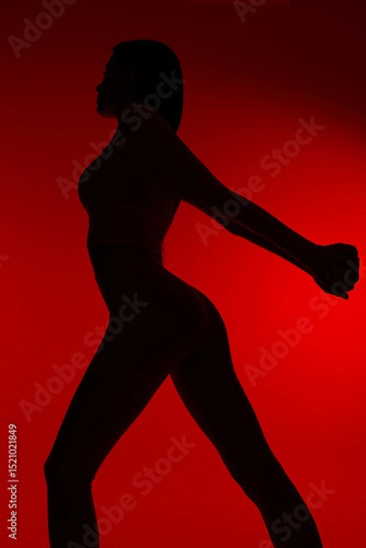 Fototapeta silhouette of a woman sport fitness stretching her arms and legs with a red background, emphasizing strength, health and active lifestyle in dynamic motion