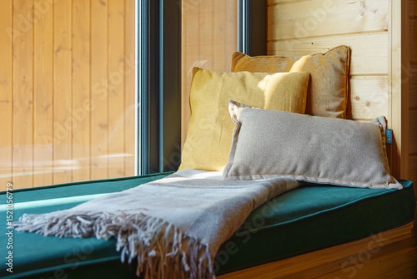 Fototapeta Comfortable seating nook features soft cushions and warm blanket, illuminated by natural light. The wooden walls create rustic yet inviting atmosphere perfect for relaxation. Home interior detail
