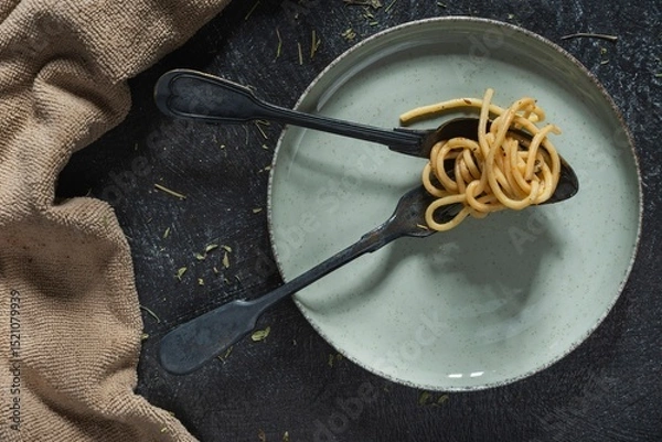 Fototapeta Still life - pasta in a plate and a fork with a spoon on the table. Food on a dark background
