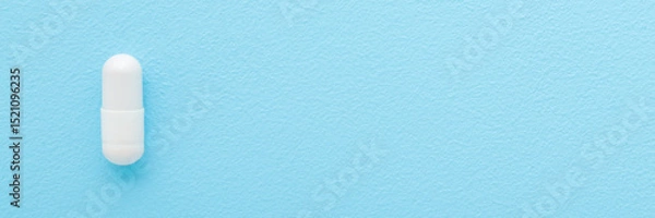 Fototapeta White capsule pill on light blue table background. Pastel color. Closeup. Wide banner. Empty place for text. Top down view.
