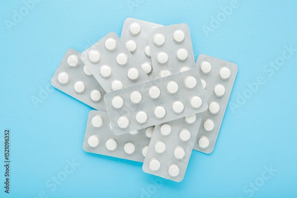 Fototapeta New blister packs of white pills on light blue table background. Pastel color. Closeup. Top down view.