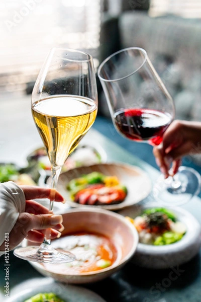 Fototapeta Two people clinking glasses of white and red wine over a table with various dishes, creating a celebratory and elegant dining atmosphere